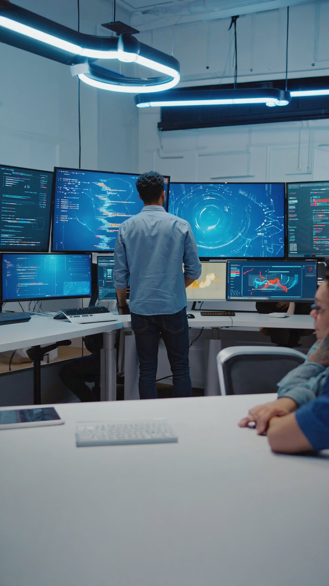 Software engineer working across a large multi-monitor setup with engineering code and 3D models
